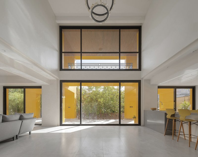 Living space with stacked horizontal windows framing yellow exterior walls and courtyard trees in daylight