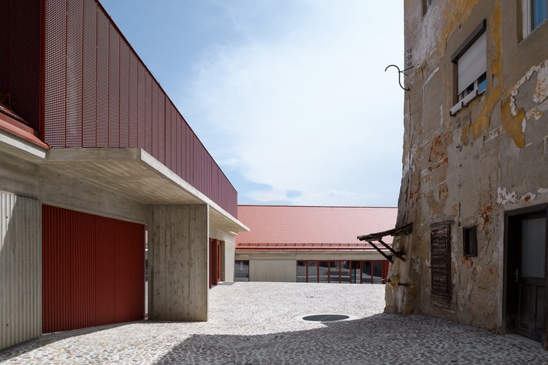 Courtyard with perforated red metal cladding on new volumes beside a weathered masonry wall