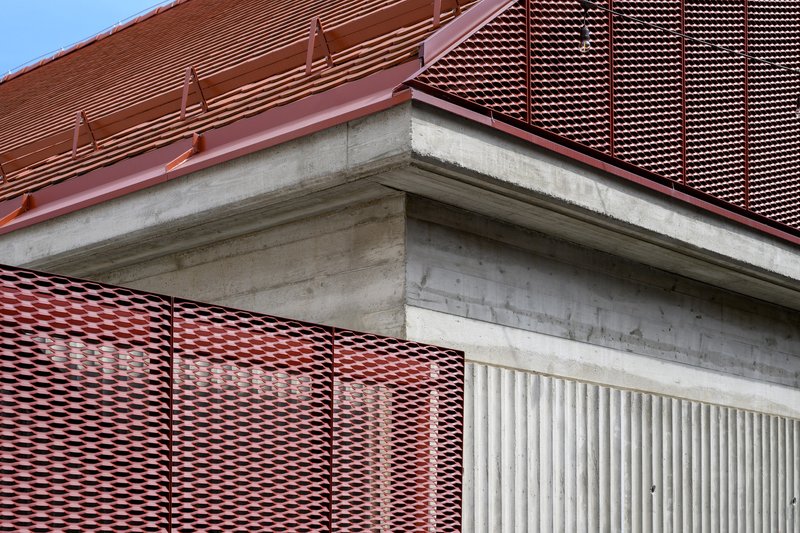 Detail of corrugated red metal roofing meeting concrete edge and perforated metal screen panels
