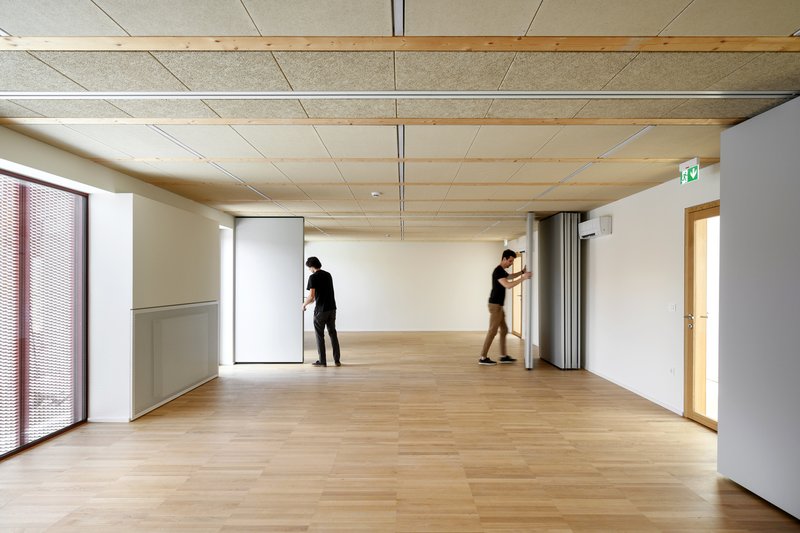 Interior room with timber ceiling panels and blonde wood flooring as two people adjust partitions