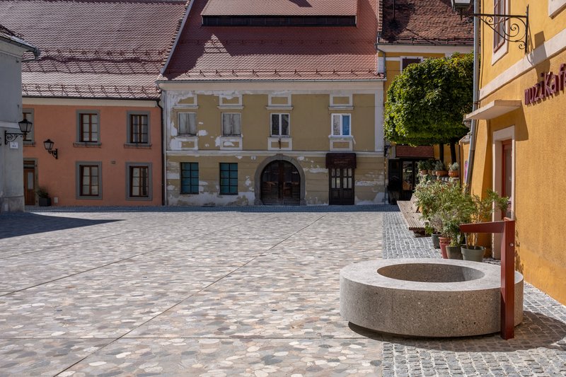 Town square with patterned paving, circular concrete fountain, and facades with orange and pink render