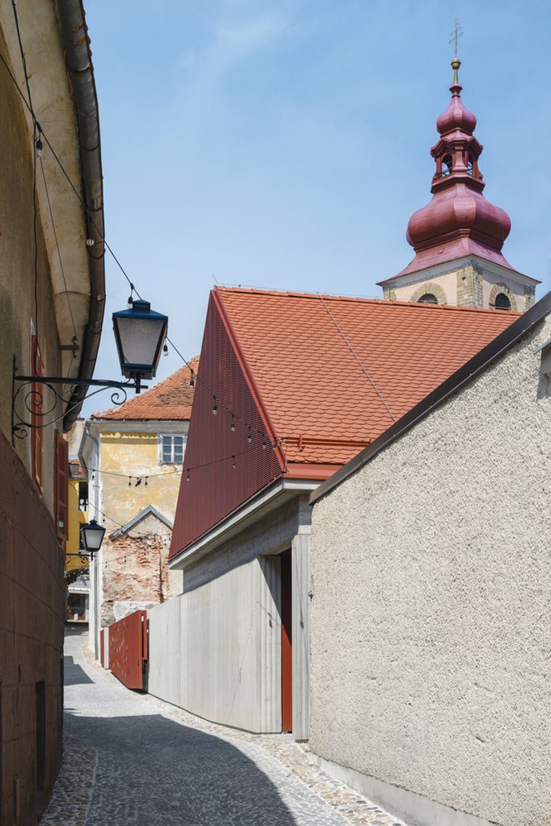 Narrow street view with white-painted timber facade beside stucco walls and church tower with orange tiles