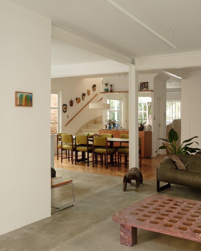 Interior view through white columns toward dining area with timber staircase and yellow chairs