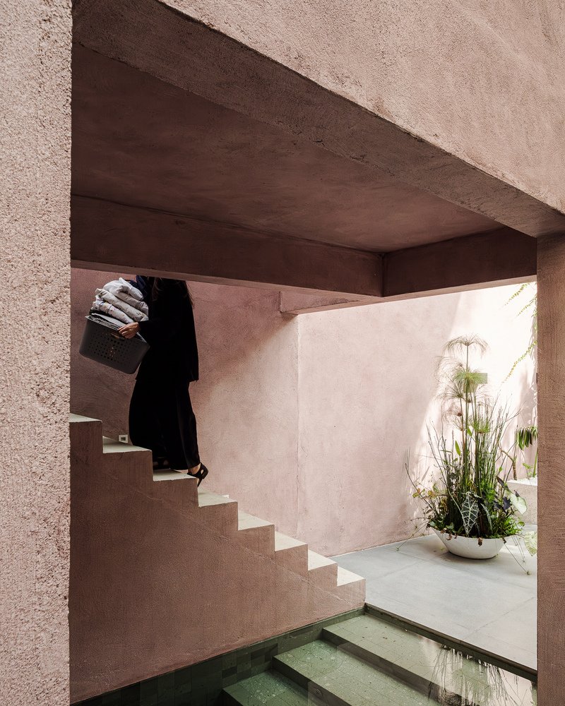 Person ascending the exterior staircase beneath the angled concrete soffit and pink stucco walls