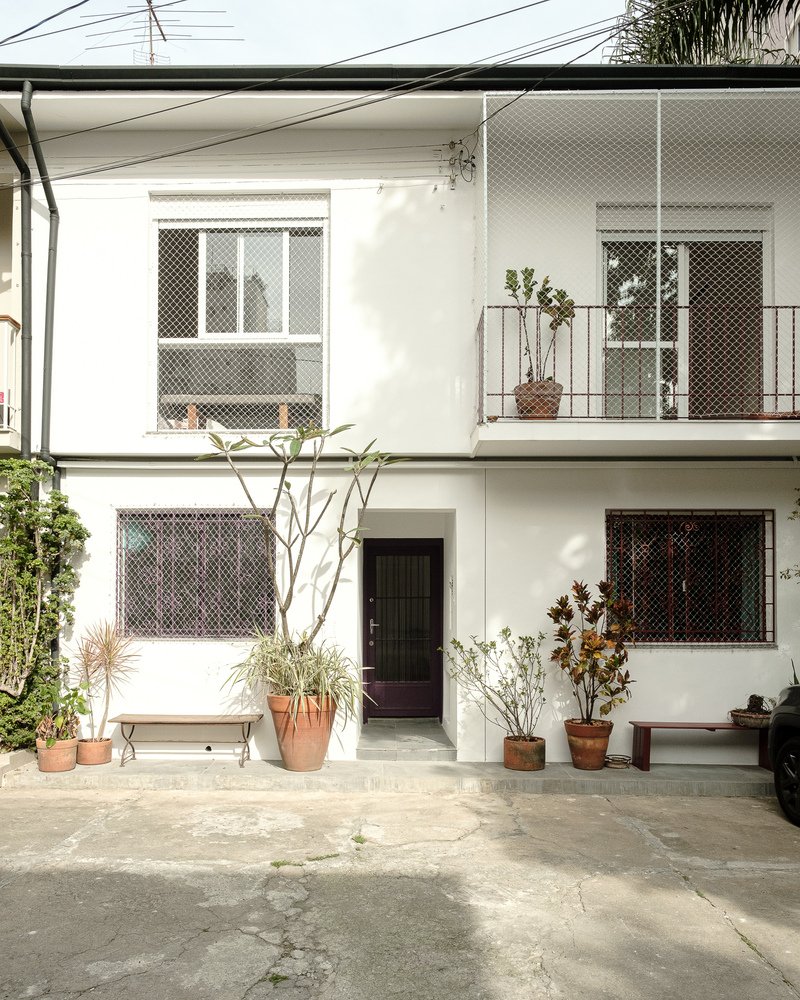 White facade with mesh-screened windows and balcony with terracotta planters in the courtyard below