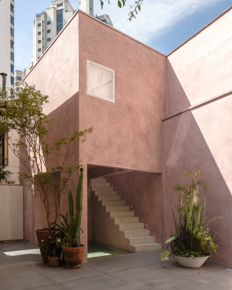 Pink stucco courtyard with exterior staircase, potted plants and high-rise towers beyond