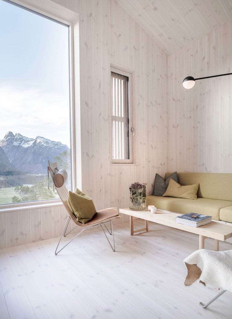 Light-filled living room with pale timber walls and corner window framing distant alpine ridges