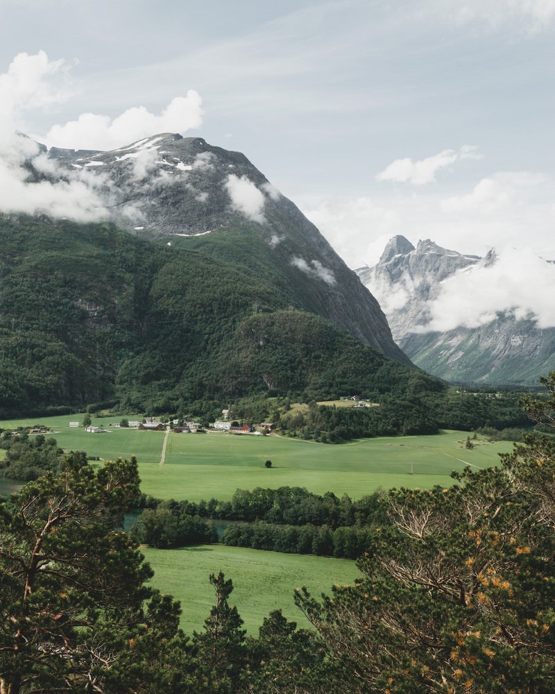 Valley view with low clouds drifting past green forested mountains in summer light