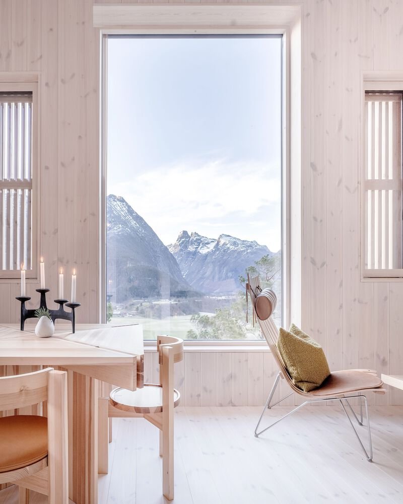 Tall fixed window with pale wood trim overlooking a fjord and snowcapped mountains at dusk