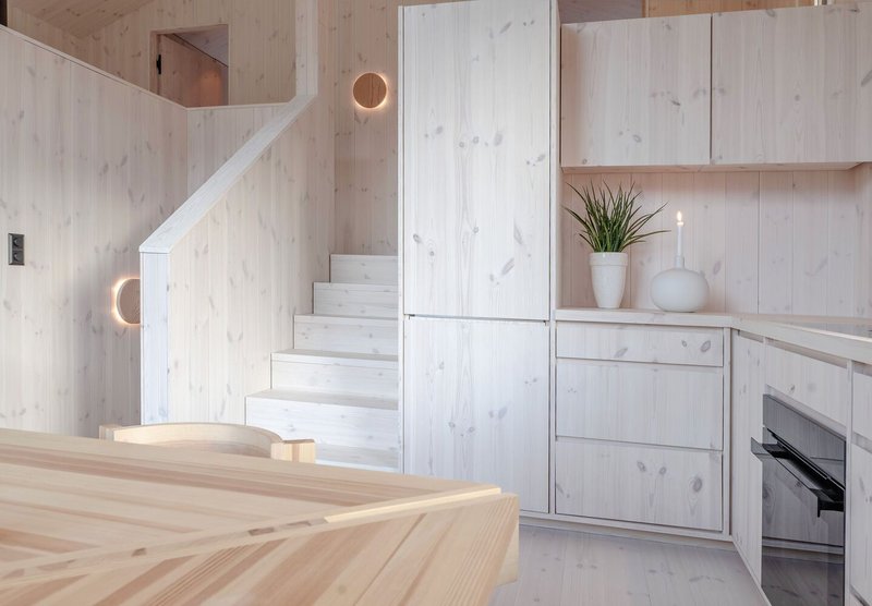 Kitchen with light wood stair rising alongside flush cabinetry and a circular wall sconce