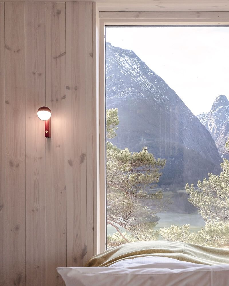 Large bedroom window with vertical timber cladding overlooking mountain valley and trees in daylight
