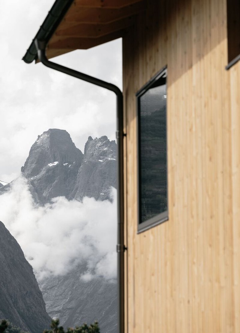 Exterior corner with timber cladding and metal gutter revealing rocky peaks through low clouds