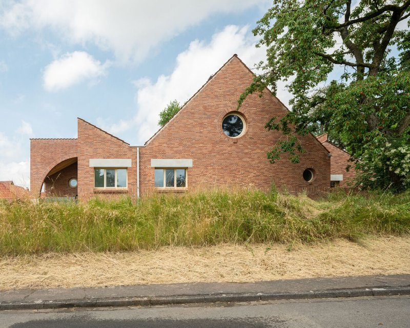 Red brick facade with gabled volumes and circular windows set behind a sloped grass berm