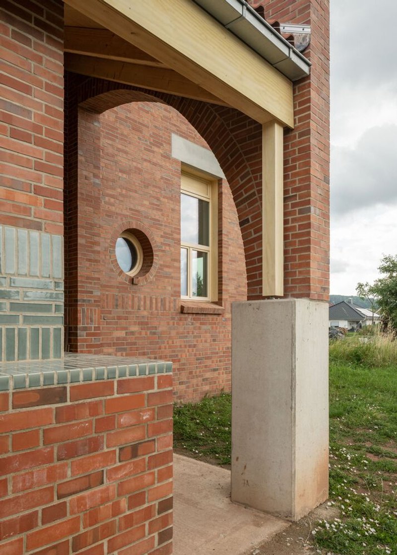 Arched brick opening with circular window and timber fascia detail supported by a concrete plinth