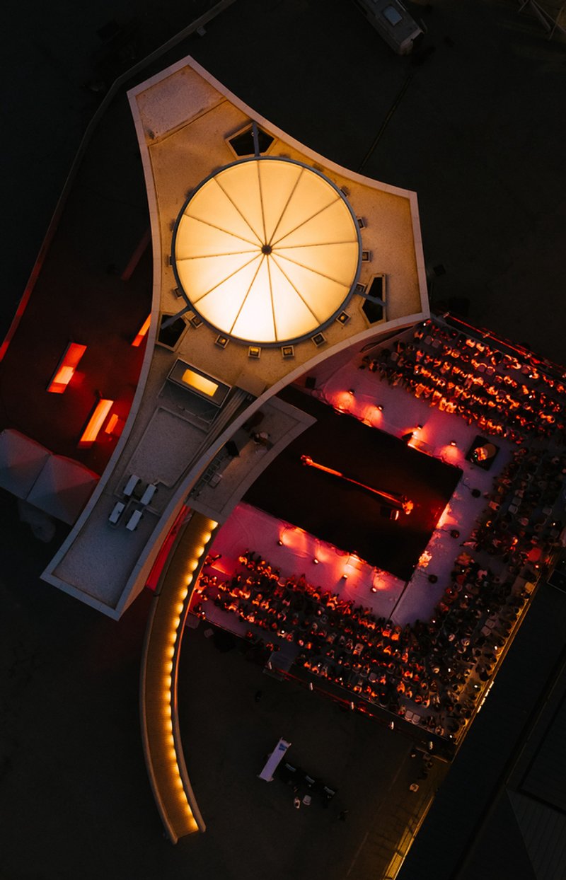 Aerial view of illuminated auditorium with radial ceiling and curved seating filled with audience at night