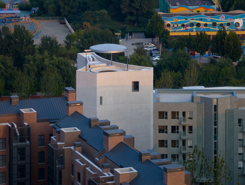Rooftop view showing disc-shaped canopy atop tower volume among residential buildings at dusk
