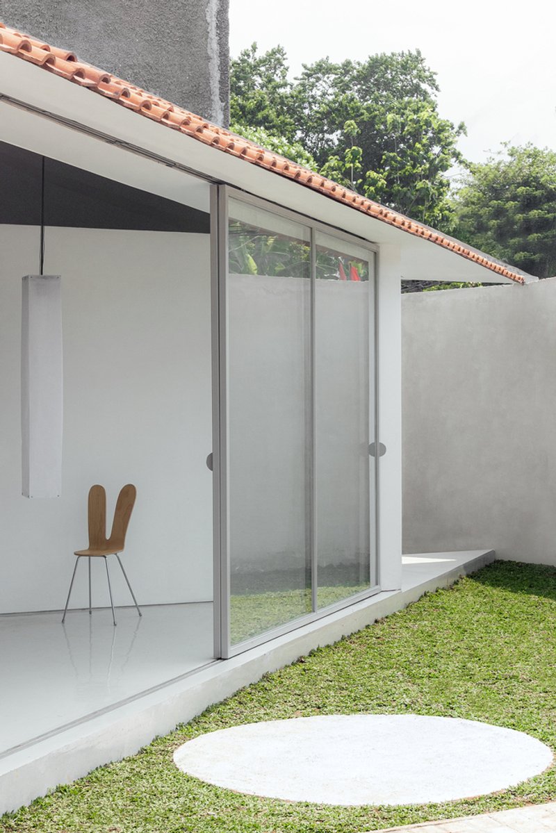 Exterior facade with sliding glass panels, terra-cotta roof and a circular disk in the lawn
