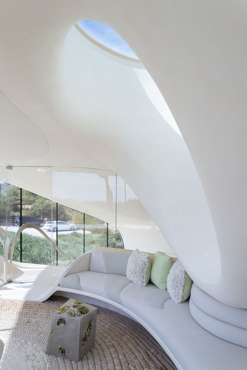 Interior living space with curved white walls and a teardrop-shaped skylight washing light across the ceiling