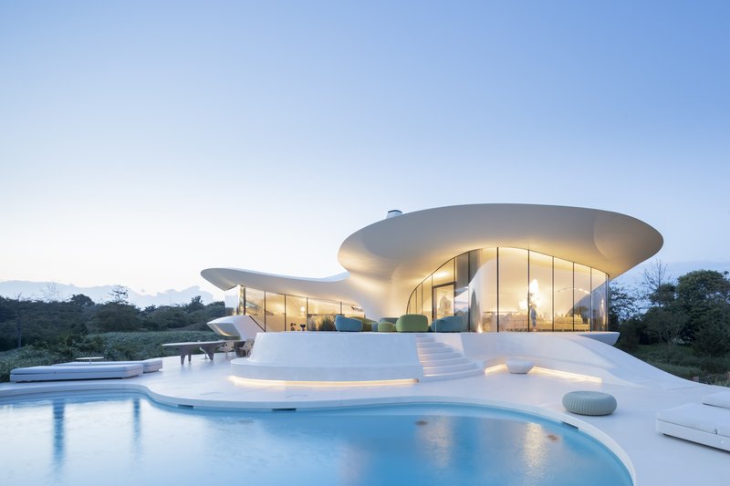 Exterior view at dusk showing the layered cantilevered roof planes and terrace pool glowing with interior light
