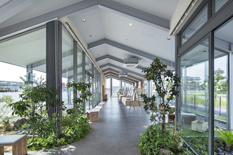 Interior corridor with exposed beam ceiling, glass walls, and planted beds along the polished floor