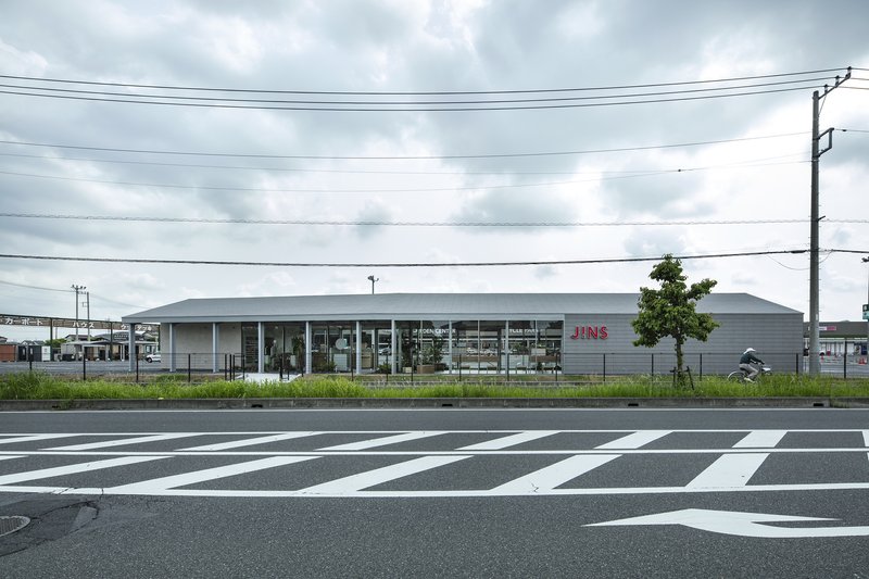 Street view of the low horizontal volume with glazed facade and striped pedestrian crossing in foreground