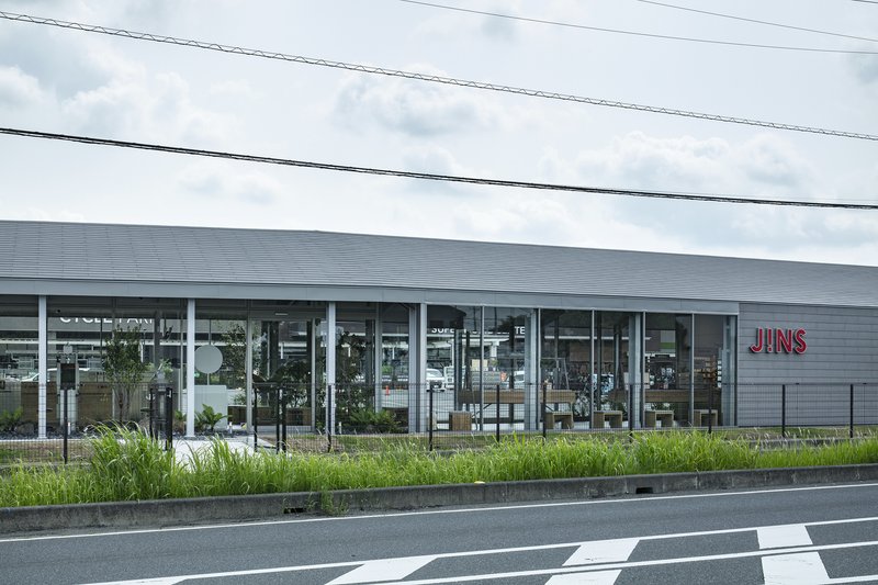 Glazed facade with slender white columns and planted bed along the roadside under overcast sky