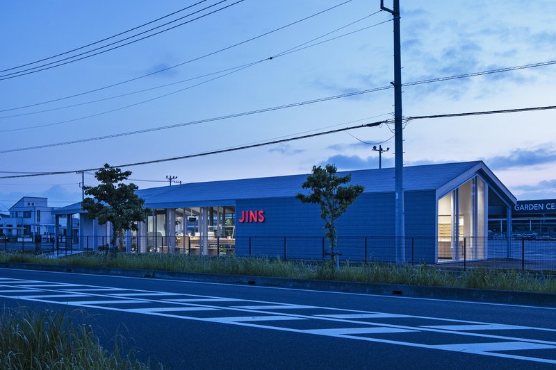 Blue metal-clad retail building with glazed storefront viewed from across the road at dusk