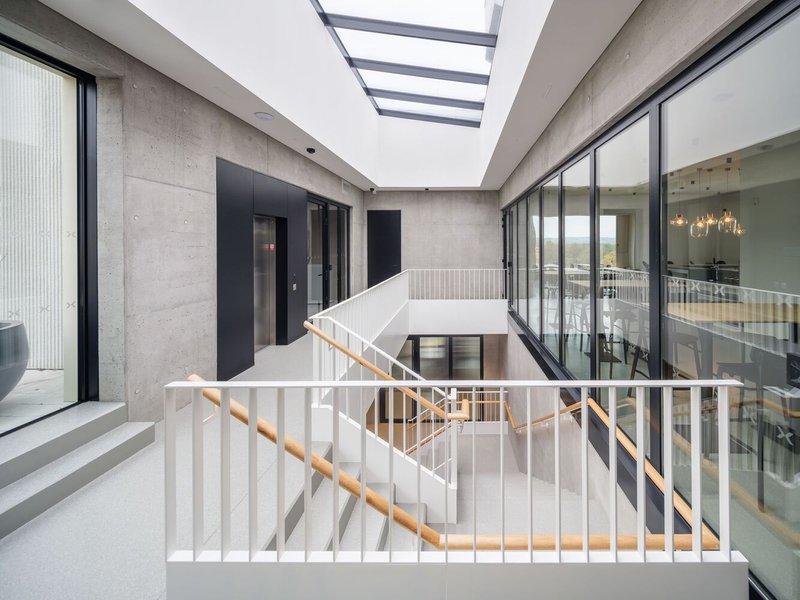 Interior stairwell with white metal railings and timber handrail beneath a slatted skylight