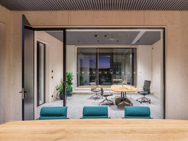 View through glass partitions from one meeting room into another with plywood walls at dusk