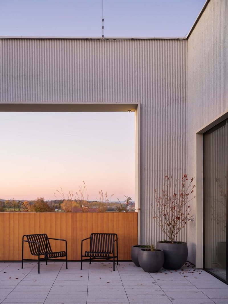 Rooftop terrace with two metal chairs and planted pots framed by corrugated metal walls at dusk