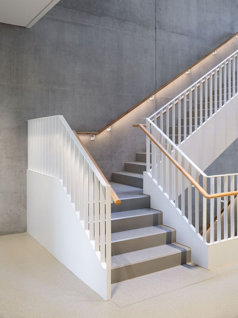 White-painted timber staircase with vertical slat railings ascending against a board-formed concrete wall with integrated lighting