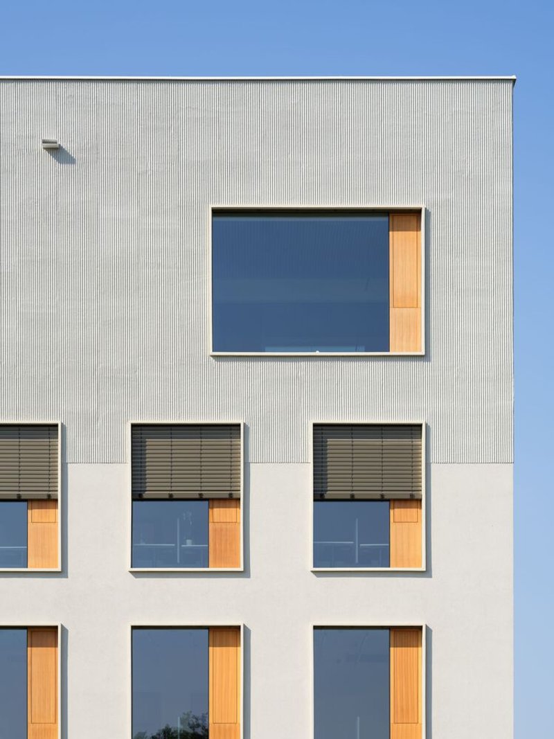 Facade detail showing corrugated metal cladding above smooth render with timber-lined window openings and exterior blinds