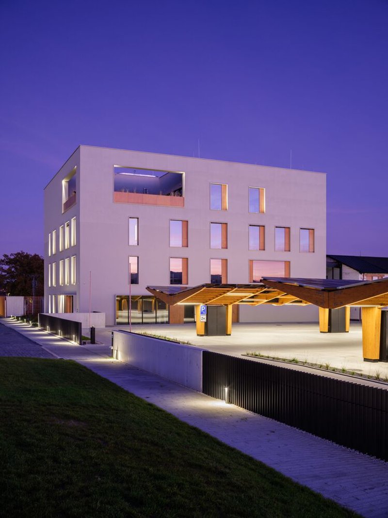 Timber pergola canopy with illuminated columns beside the building at twilight