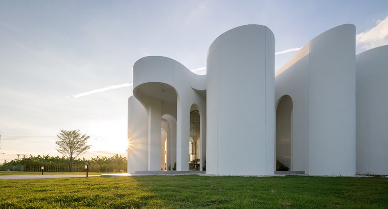 White cylindrical volumes with arched openings surrounding a lawn at sunset