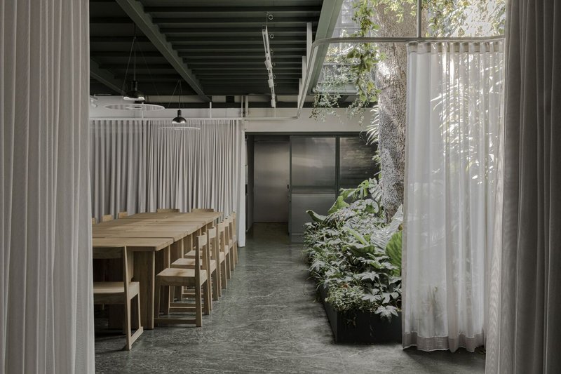 Dining area with timber table and stools framed by sheer curtains and an indoor planted bed