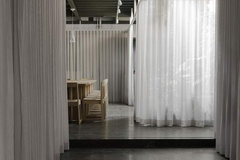 Corridor view through layered sheer curtains with timber furniture and exposed structural ceiling above