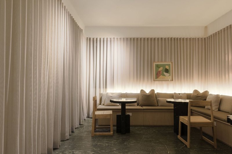 Seating alcove with timber benches and black side tables enclosed by floor-to-ceiling sheer curtains