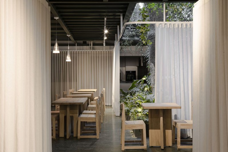 Dining hall with timber tables and benches under exposed beam ceiling with planted courtyard visible beyond