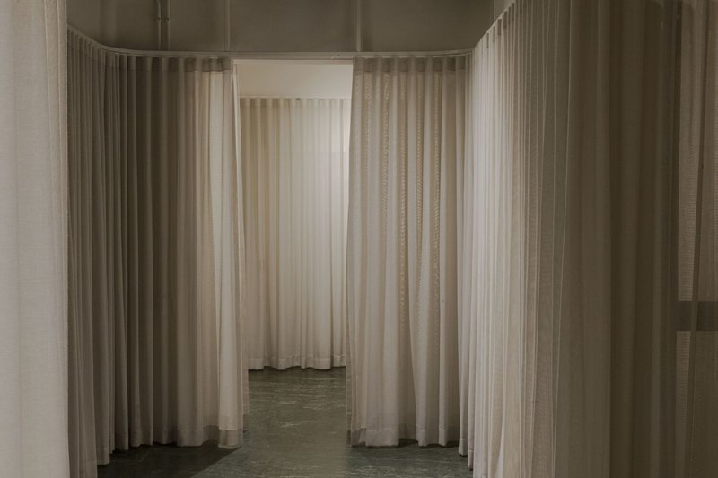 Corridor view framed by sheer white curtains hung from ceiling tracks on polished concrete floors