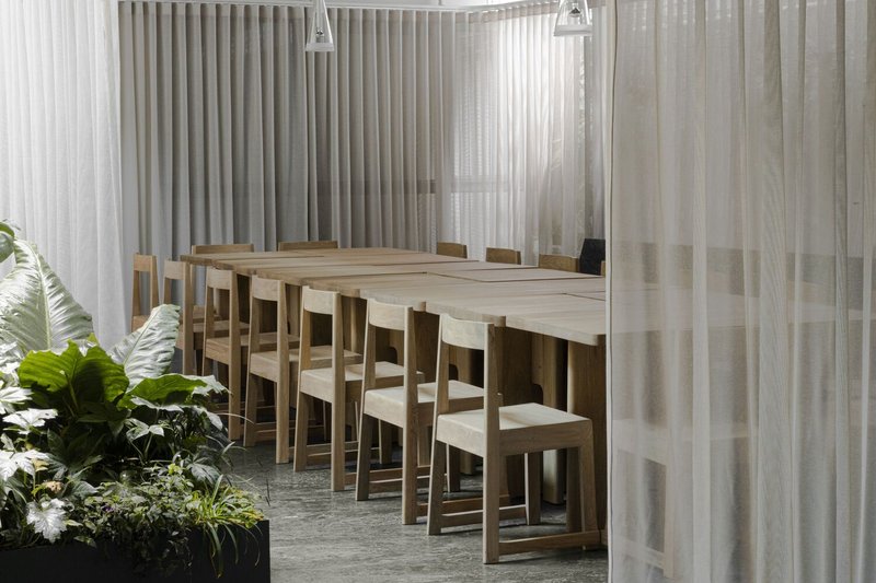 Timber dining table and chairs surrounded by translucent curtain partitions with potted plants in foreground