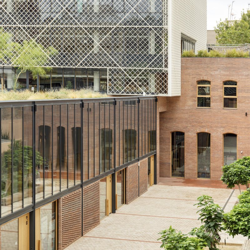 Courtyard view showing diagonal mesh facade cantilevering over retained brick facade with arched openings