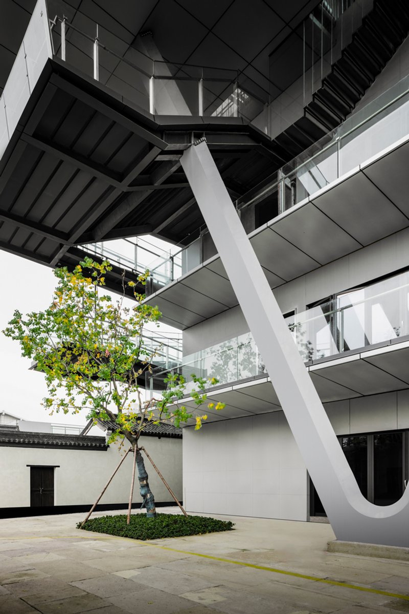 Courtyard with angled white structural column supporting tiered floors and a small planted tree bed below