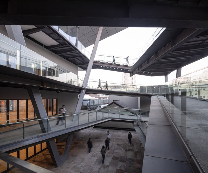 Multi-level interior courtyard with exposed steel bridges connecting glazed galleries as visitors gather below at dusk