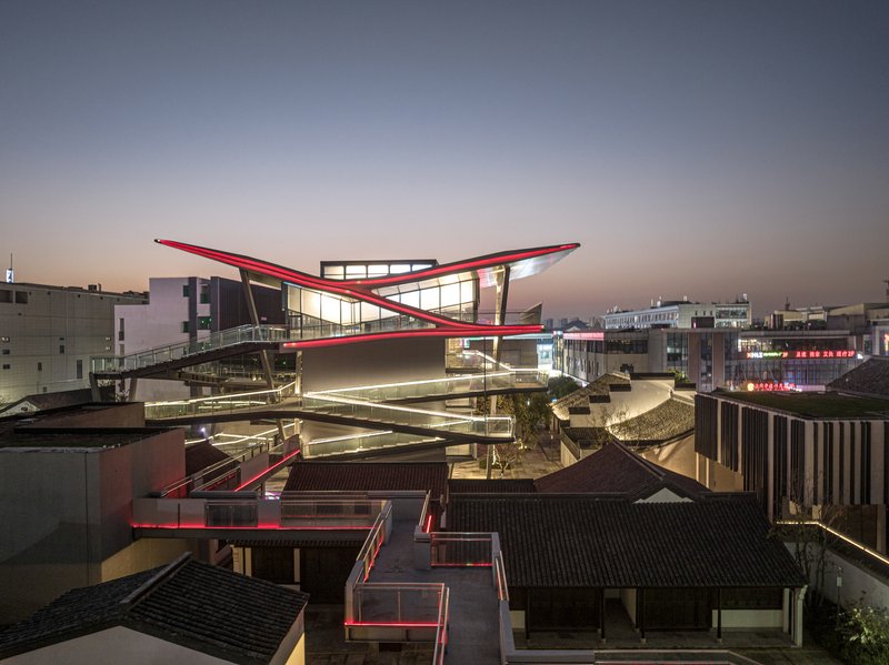 Night view of the illuminated winged roof rising above preserved traditional tile-roofed structures and pathways