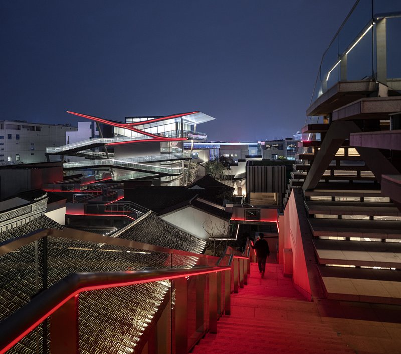 Red-lit exterior staircase descending past railings toward courtyard buildings under evening sky