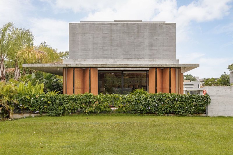 Front facade with board-formed concrete volume above timber-clad ground floor and manicured hedge