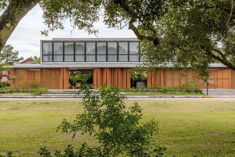 Garden view showing the glazed upper volume and timber facade beneath overhanging tree branches