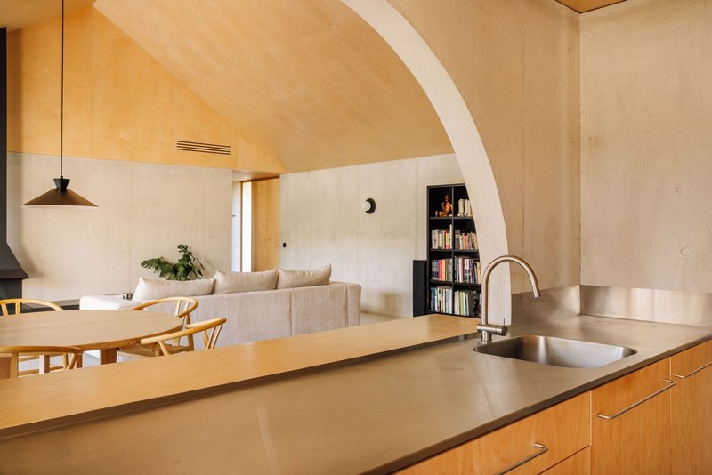 Open kitchen with timber cabinetry and stainless steel countertop beneath arched plywood ceiling with recessed vent grille