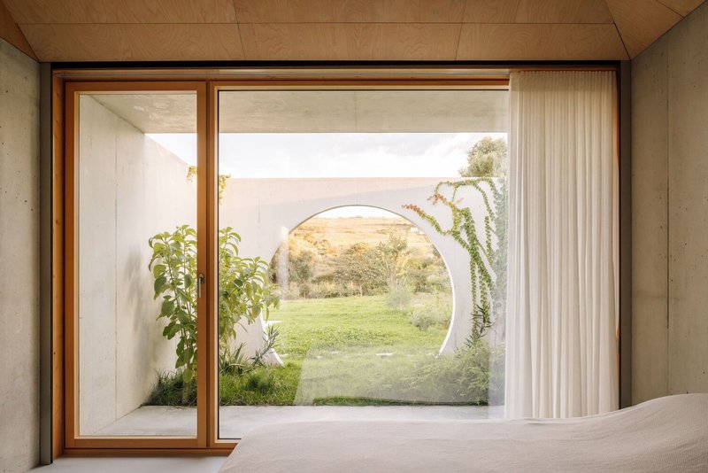Bedroom view through sliding timber-framed glazing to courtyard with circular moon gate opening onto lawn at dusk