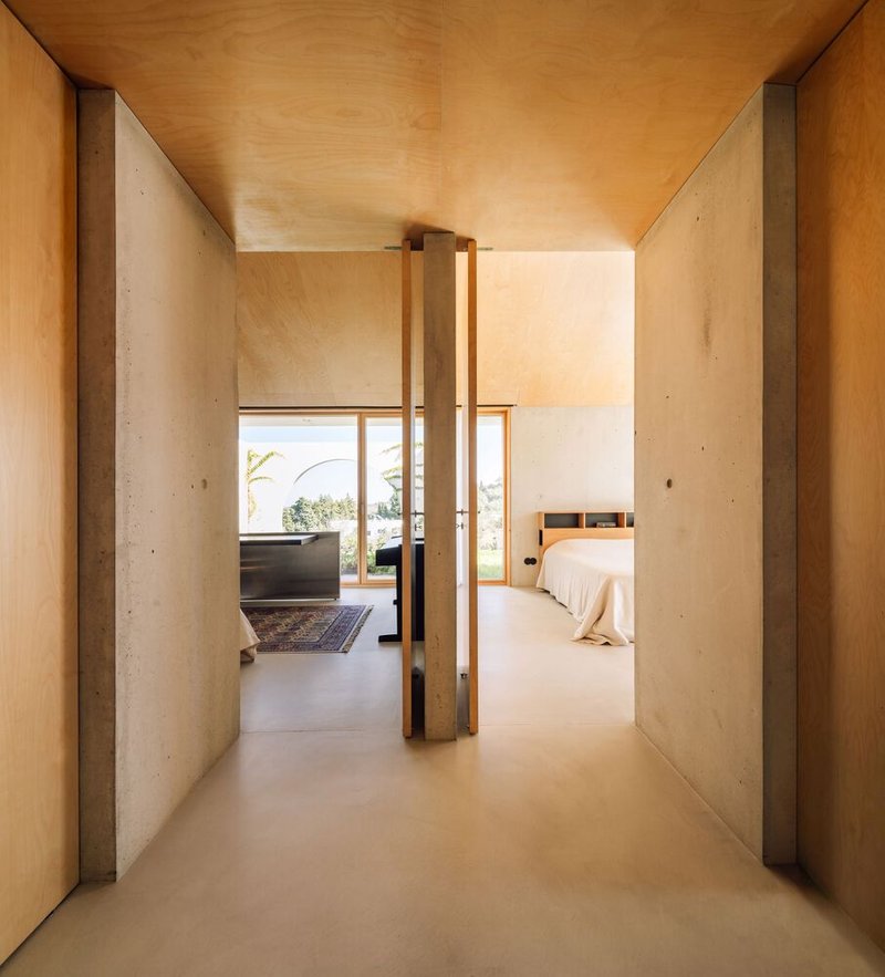 Hallway with timber-framed door, concrete walls, and plywood ceiling leading to bedroom suite